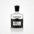 Creed Aventus Eau de Parfum bottle on a reflective white surface. The clear glass bottle features a textured black lower section with a silver label, and a black cap.