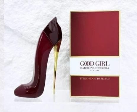 A Carolina Herrera Good Girl perfume bottle shaped like a high-heeled stiletto shoe in glossy deep burgundy with a gold heel, displayed next to its red and white packaging box.